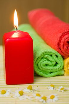 An image of a burning candle, towels and chamomiles
