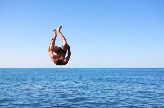 Young strong man doing somersault between blue sky and sea