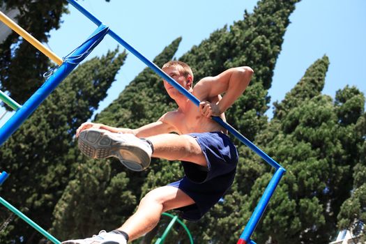 Young strong teenage athlete doing exercise on horizontal bar