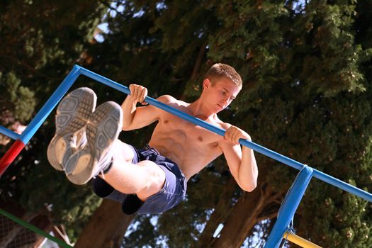 Young strong teenage athlete doing pull-up on horizontal bar