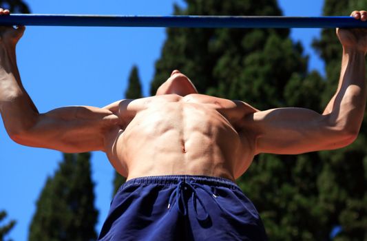 Closeup of young strong teenage athlete doing pull-up on horizontal bar