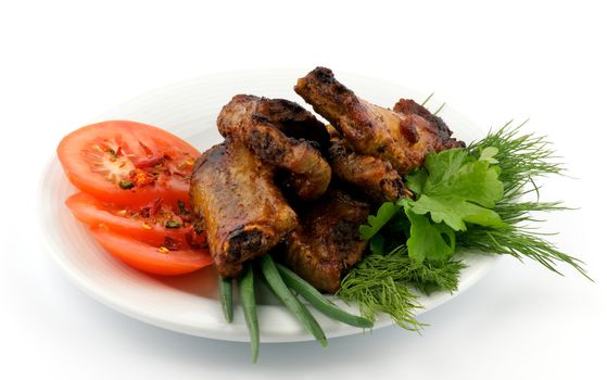 Barbecued pork ribs with tomato and greens on plate isolated on white background