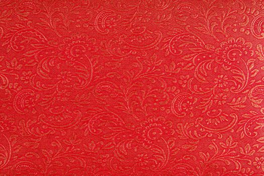 A background of a red fabric with an ethnic Indian design in gold.