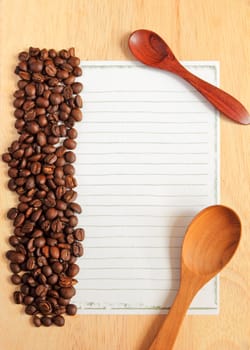 Coffee beans and spoon with paper for notes on the wooden background