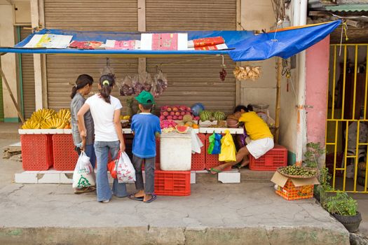 A Filipino family shopping for fruit at a roadside stand in Bogo City while the owner sleeps at her table. Laid back Asian style of doing business.