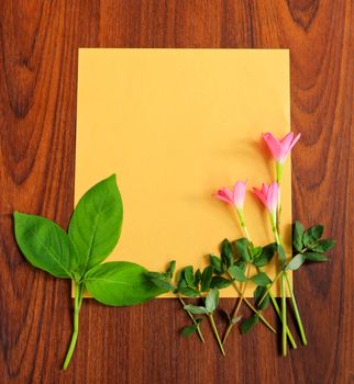 Flowers and leaves with yellow paper on wooden background