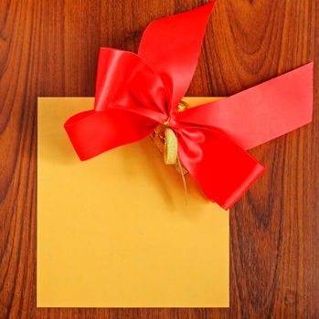 Notepaper with red bow on wooden background