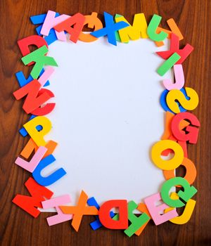 Colorful alphabet as frame with white paper on wooden background