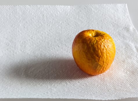 Old wrinkled apple sitting on a white paper sheet with sidelighting and shadow