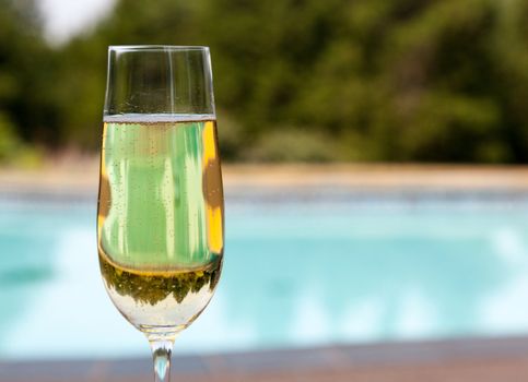 Elegant flute glass of sparkling white wine or champagne by side of swimming pool