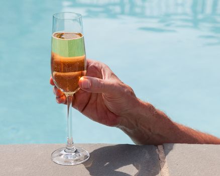 Elegant flute glass of sparkling white wine or champagne being held from in pool
