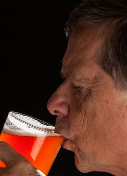 Senior caucasian man in profile drinking from a pint glass of beer or lager