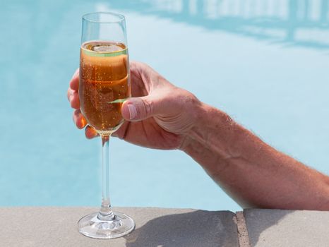 Elegant flute glass of sparkling white wine or champagne being held from in pool