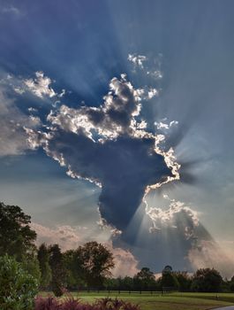 HDR shot of a tall anvil shaped cloud over meadows with sunrays