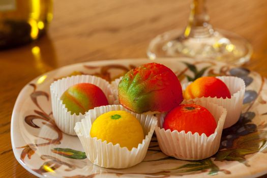 Fruit shaped candies in macro image of marzipan sweets on table with glass and bottle of wine