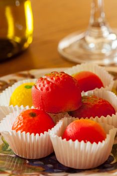 Fruit shaped candies in macro image of marzipan sweets on table with glass and bottle of wine