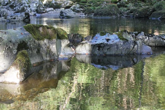 A stretch of river in the fall with water polished rocks and bright reflections of the trees.