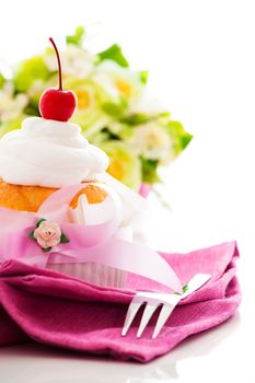 Muffin on a pink napkin cream and cherry on the top with flower in the background as a studio shot