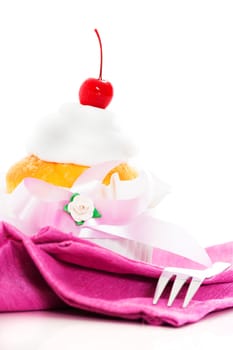 Muffin on a pink napkin cream and cherry on the top. White background as a studio shot