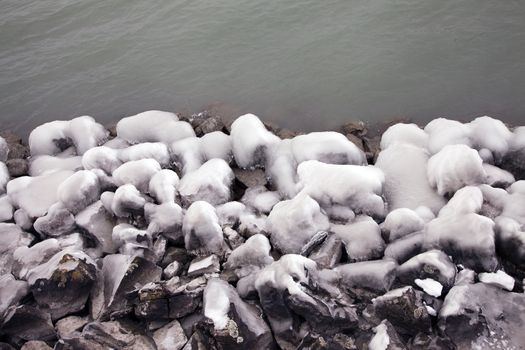 Heavy winter weather deposits ice on rocks by the lakeside