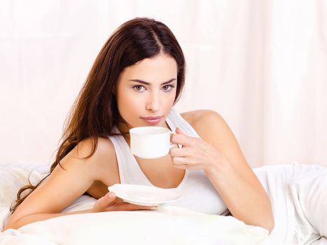 Pretty woman holding cup of coffee in bed