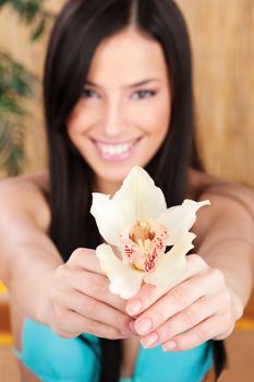 Pretty smiled woman holding white orchid in bikini, focus on flower