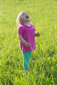 Joyful baby girl looking up among grass