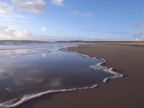 Very popular tourist beach, Newborough, Anglesey, Wales, UK, with the incoming tide over deserted sands with a blue sky and cloud in the distance.