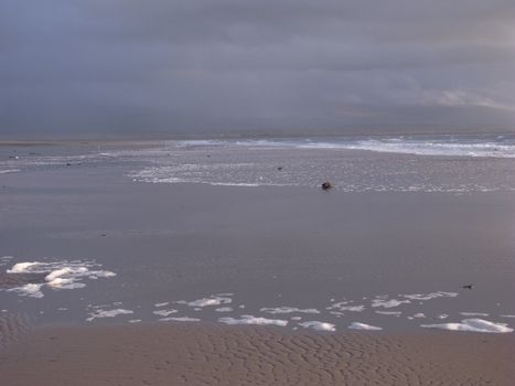 A sandy beach with the incoming tide and storm clouds over the mountains in the distance.