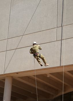 guy in defence force camouflage fatigues abseiling down a wall