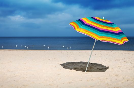 Colorful umbrella on a sandy beach, peaceful sea in a background