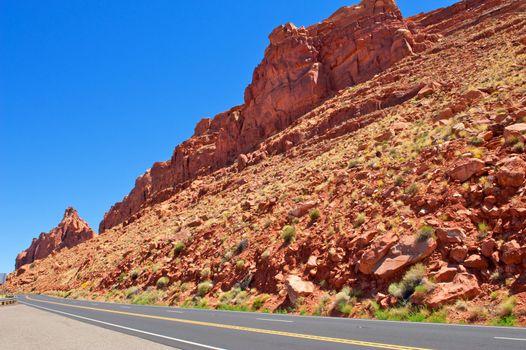 A deep blue sky and red rock cliffs sit close to a paved highway in northern Arizona