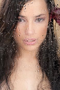 Close up of a pretty woman's face behind glass full of water drops