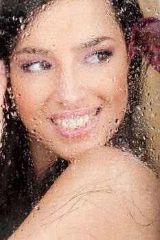 Big smile of a pretty woman behind glass full of water drops