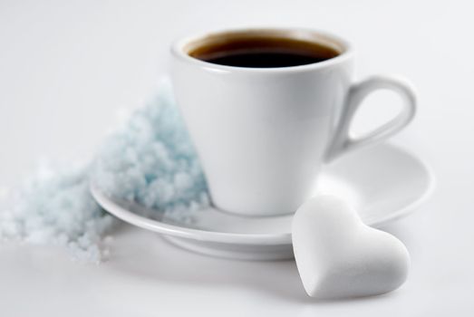 Cup of coffee with heart shaped blank candy and snow hill on saucer. Isolated on white. Small Depth of Field