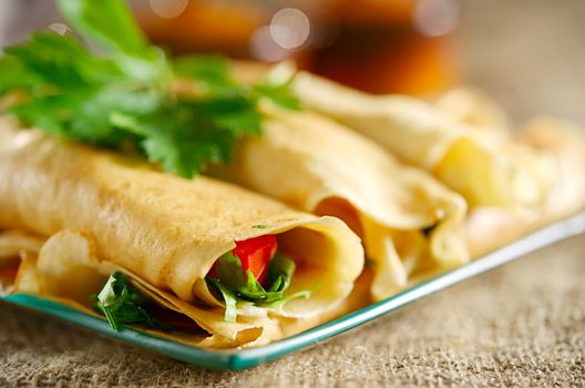 Dessert with the rolled pancakes in a glass plate on the background of canvas cloth