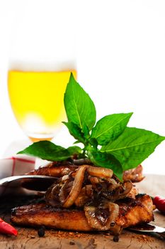 View of some pieces of spicy fried meat with onion on a wooden underground chili  pepper as decoration and a glass of beer im the background