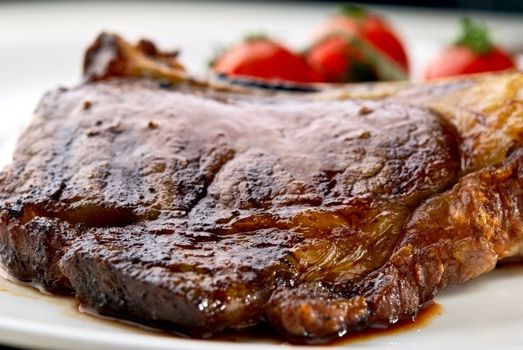 Club Steak. Veal on the bone. Macro of grilled meat ribs on white plate with cherry tomatoes and dark hot sauce