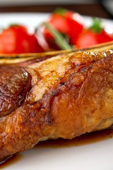 Club Steak. Veal on the bone. Macro of grilled meat ribs on white plate with cherry tomatoes and dark hot sauce