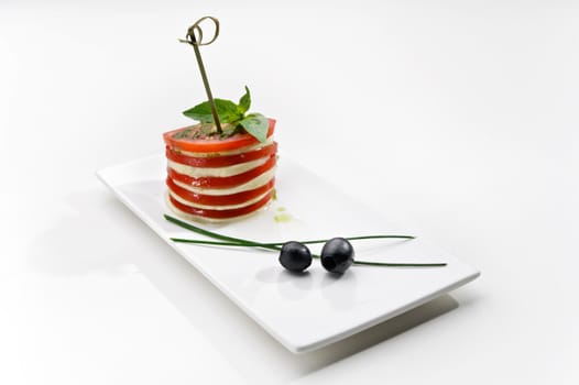 Delicious canape with tomato and cheese served with olive on white plate