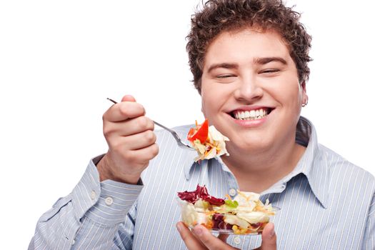 Happy young chubby man eating fresh salad with fork, isolate on white