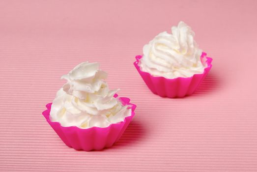 Two portions of whipped cream over pink background. Shallow DOF