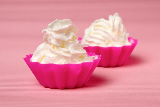 Two portions of whipped cream over pink background. Shallow DOF