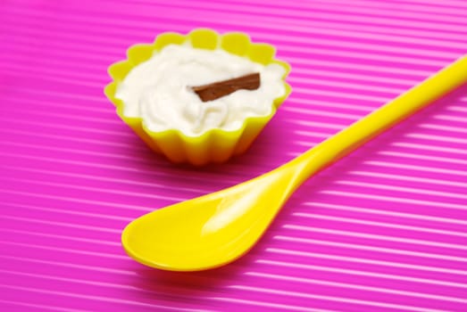 Empty yellow spoon with portion of whipped cream and chocolate over pink background. Shallow DOF