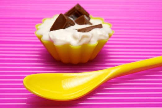 Empty yellow spoon with portion of whipped cream and chocolate over pink background. Shallow DOF