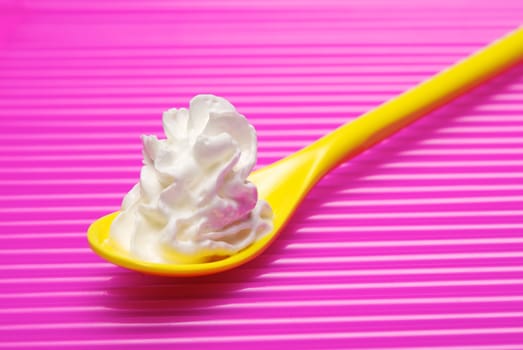 Yellow spoon full of whipped cream over pink background. Shallow DOF