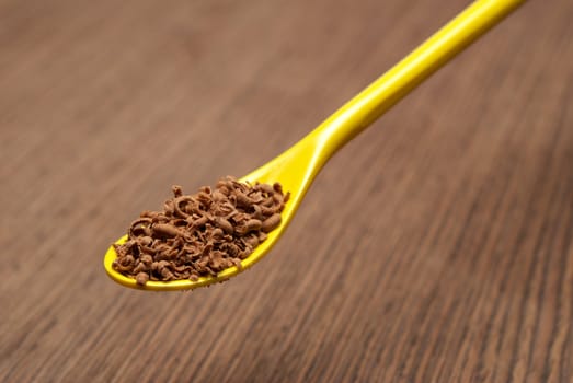 Teaspoon full of chocolate shavings, on a wooden background closeup