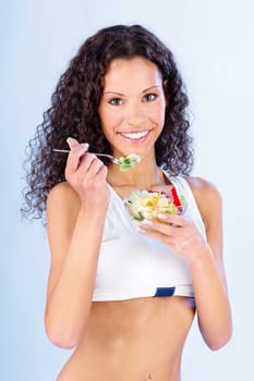Pretty fitness woman holding salad on fork and plate