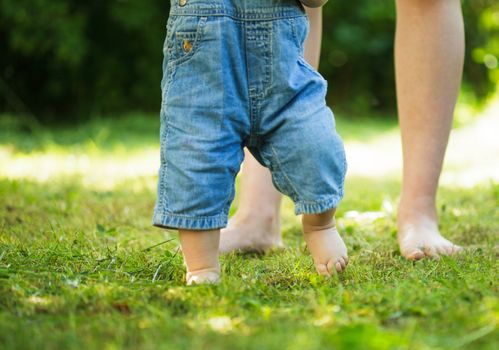 First steps of baby from mother on grass