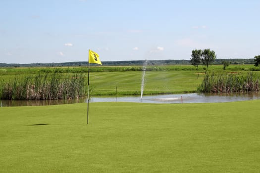 golf field with yellow flag and pond